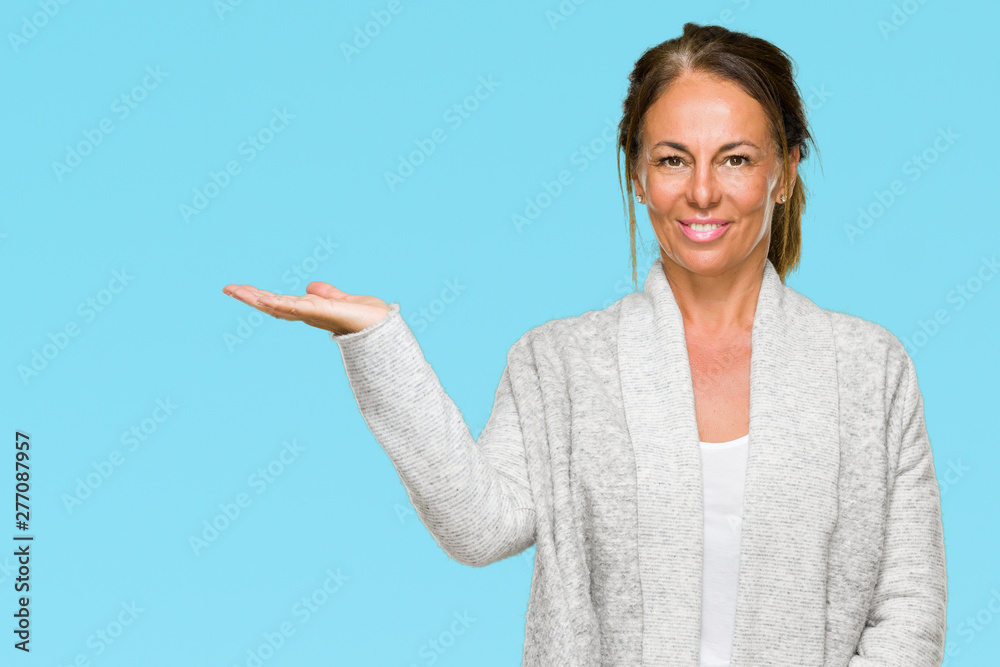 Beautiful middle age adult woman wearing winter sweater over isolated background smiling cheerful presenting and pointing with palm of hand looking at the camera. Beautiful middle age adult woman wearing winter sweater over isolated background smiling cheerful presenting and pointing with palm of hand looking at the camera.