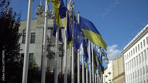 Two flags of Ukraine and the European Union are fluttering in the wind on the sky background. The concept of cooperation, friendship between Ukraine and the EU