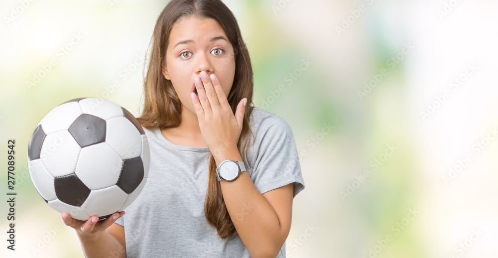 Fototapeta premium Young beautiful brunette woman holding soccer football ball over isolated background cover mouth with hand shocked with shame for mistake, expression of fear, scared in silence, secret concept