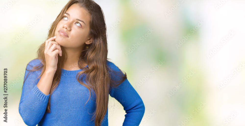 Young beautiful brunette woman wearing blue sweater over isolated background with hand on chin thinking about question, pensive expression. Smiling with thoughtful face. Doubt concept.