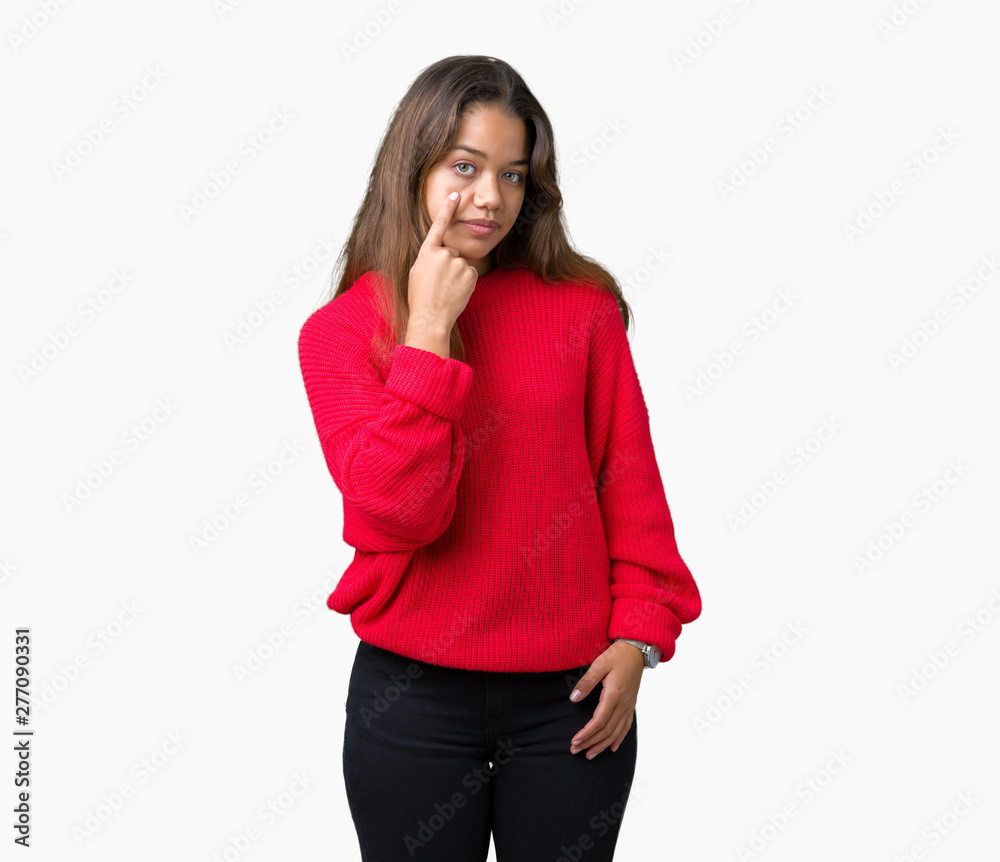 Young beautiful brunette woman wearing red winter sweater over isolated background Pointing to the eye watching you gesture, suspicious expression Young beautiful brunette woman wearing red winter sweater over isolated background Pointing to the eye watching you gesture, suspicious expression