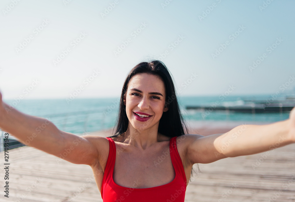 Portrait of young smiling woman in a red swimsuit takes a selfie on the beach Portrait of young smiling woman in a red swimsuit takes a selfie on the beach