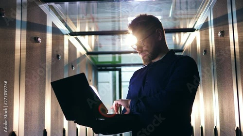 Computer system security specialist. A man stands in a server room, working with a laptop. photo