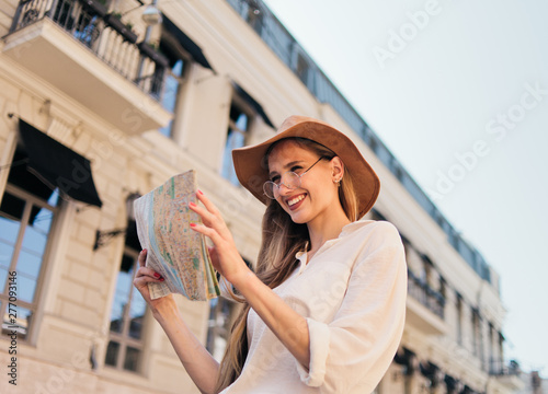 Obraz na płótnie Young casual style tourist woman in felt hat looking into the city map against the background of old urban architecture