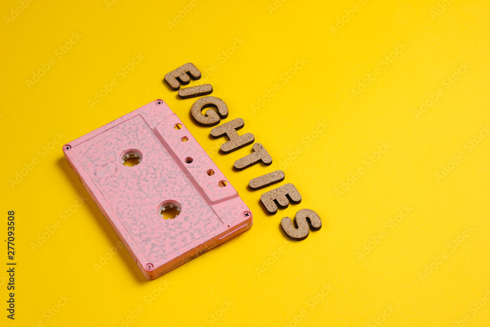 Creative retro style concept, 80s. Audio cassette on yellow background with the word Eighties from wooden letters, minimalism Creative retro style concept, 80s. Audio cassette on yellow background with the word Eighties from wooden letters, minimalism