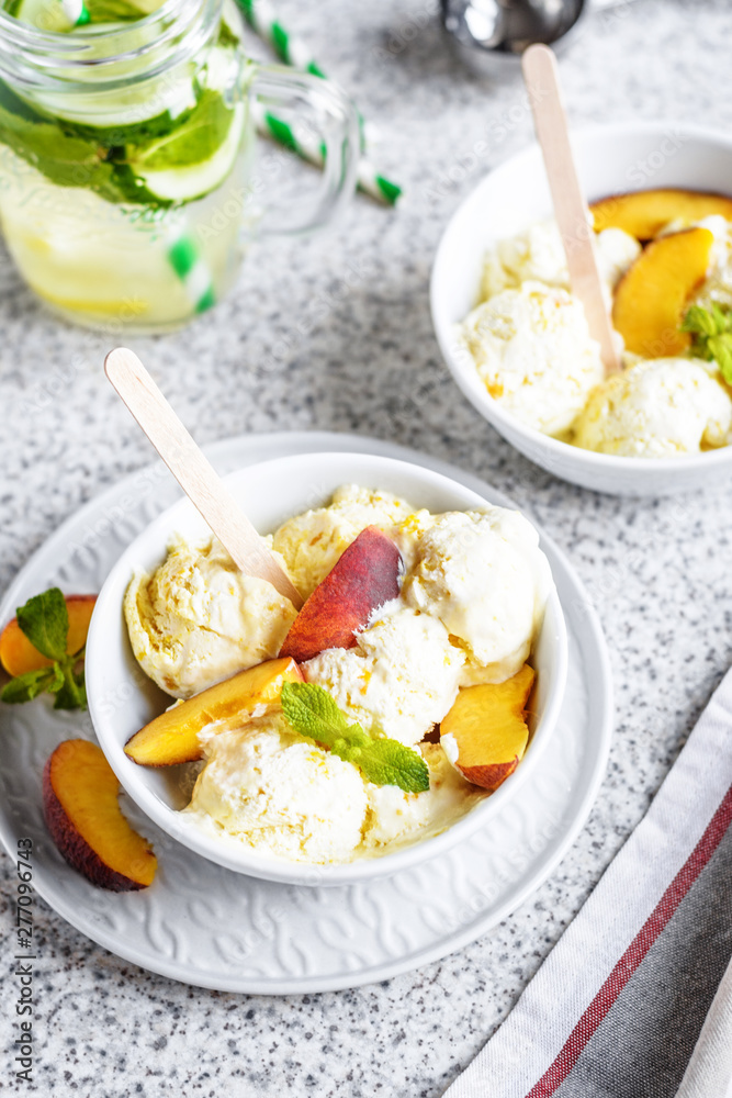  Homemade peach ice cream with mint and fresh peach slices in a plate on a gray background