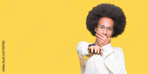 Young african american man with afro hair wearing glasses Laughing of you, pointing to the camera with finger hand over mouth, shame expression