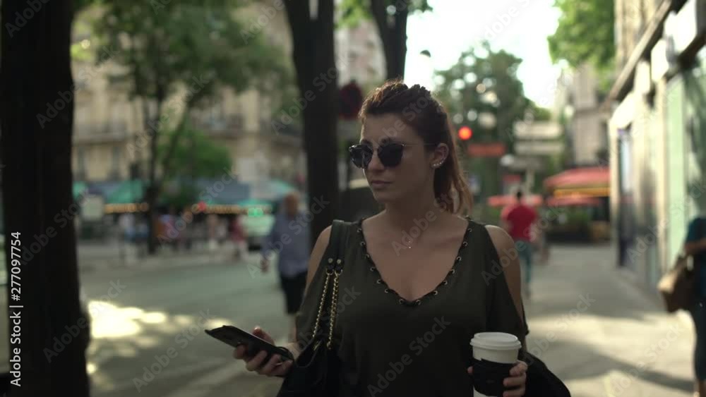 Attractive caucasian woman with sunglasses, freckles, piercings and red hair scrolling social media on her smartphone walking through the street, during sunny summer in Paris. 4K UHD. Trendy. Attractive caucasian woman with sunglasses, freckles, piercings and red hair scrolling social media on her smartphone walking through the street, during sunny summer in Paris. 4K UHD. Trendy.