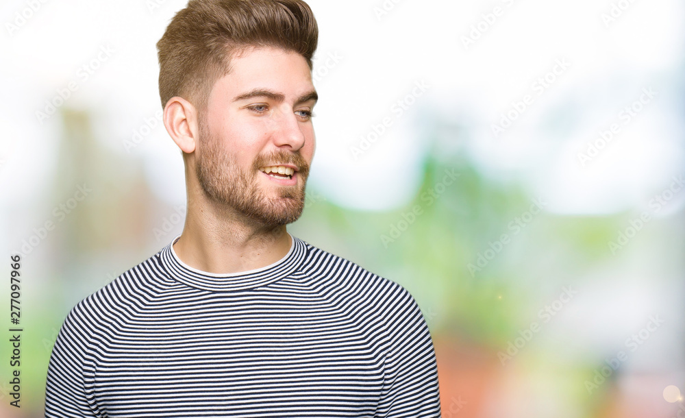 Young handsome man wearing stripes sweater looking away to side with smile on face, natural expression. Laughing confident. Young handsome man wearing stripes sweater looking away to side with smile on face, natural expression. Laughing confident.
