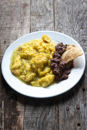 Mexican scrambled eggs in green sauce also called "al abañil" with beans on wooden background