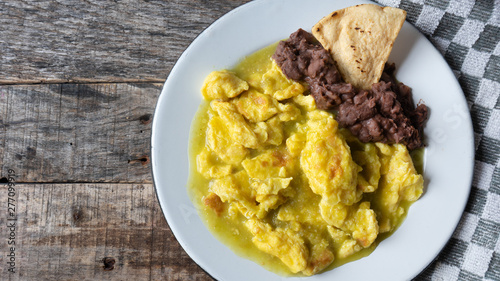 Mexican scrambled eggs in green sauce also called "al abañil" with beans on wooden background