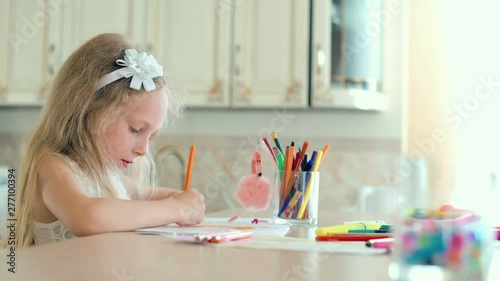 Cute little girl sits at the table and draws with pencils. photo