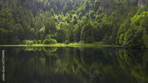 Aerial on mountain lake and green forest trees. Forest reflection in the water. Beautiful aerial landscape with lake and forest.Drone shot over a beautiful mountain forest lake.Magical atmosphere