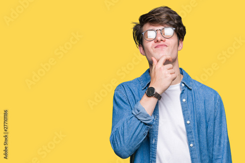Young handsome man wearing glasses over isolated background looking confident at the camera with smile with crossed arms and hand raised on chin. Thinking positive. © Krakenimages.com
