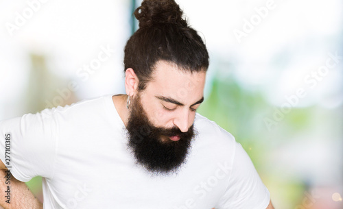 Young hipster man with long hair and beard wearing casual white t-shirt Suffering of backache, touching back with hand, muscular pain