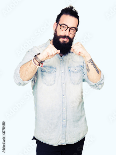 Young hipster man with long hair and beard wearing glasses Ready to fight with fist defense gesture, angry and upset face, afraid of problem
