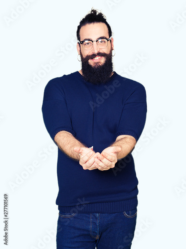 Young hipster man with long hair and beard wearing glasses Smiling with hands palms together receiving or giving gesture. Hold and protection