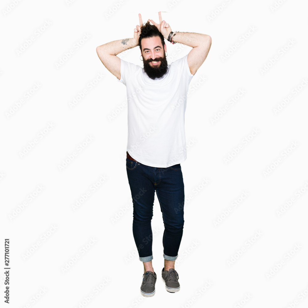 Young hipster man with long hair and beard wearing casual white t-shirt Posing funny and crazy with fingers on head as bunny ears, smiling cheerful Young hipster man with long hair and beard wearing casual white t-shirt Posing funny and crazy with fingers on head as bunny ears, smiling cheerful