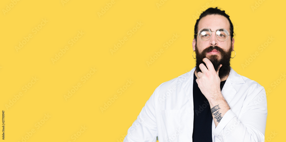 Doctor therapist man with long hair and bear wearing white coat looking confident at the camera with smile with crossed arms and hand raised on chin. Thinking positive. Doctor therapist man with long hair and bear wearing white coat looking confident at the camera with smile with crossed arms and hand raised on chin. Thinking positive.