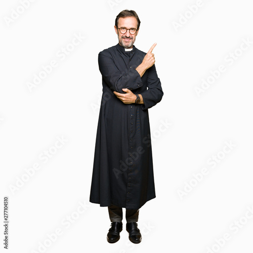 Middle age priest man wearing catholic robe Pointing with hand finger to the side showing advertisement, serious and calm face