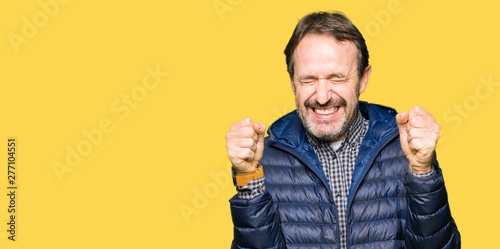 Middle age handsome man wearing winter coat excited for success with arms raised celebrating victory smiling. Winner concept.