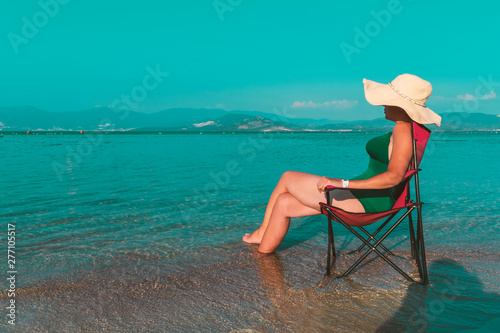 Pretty young girl sitting on a chair. Beach in the sea, bright air in her vacation in the sea of Turkey. Highlights the beautiful summer weather in swimming suit