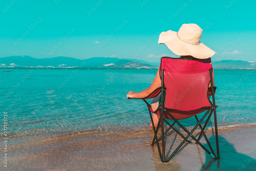 Pretty young girl sitting on a chair. Beach in the sea, bright air in her vacation in the sea of Turkey. Highlights the beautiful summer weather in swimming suit