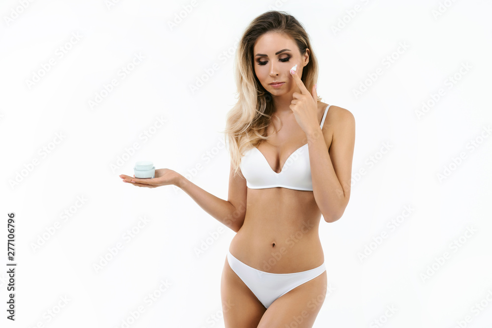Beauty perfect slim body: fit sporty and healthy woman posing at white background in underwear with facial cream on hand Beauty perfect slim body: fit sporty and healthy woman posing at white background in underwear with facial cream on hand
