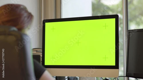 Redhead Woman working on personal computer with Mock-up Green Screen in her studio. Attractive and gorgeous woman with red hair, Internet, multi monitors, hacking, freelance, motion designer.