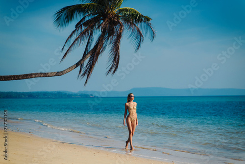 Pretty woman in sexy golden swimsuit and sunglasses posing at the beach and palm tree background
