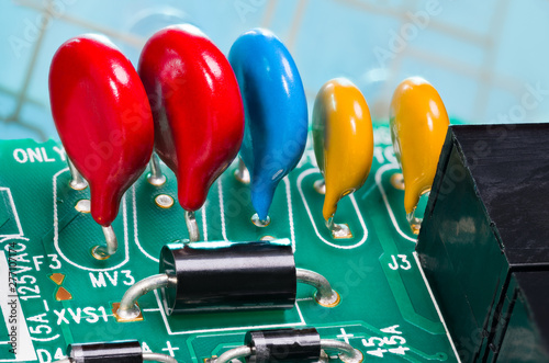 Colorful varistors. Circuit board detail. Electronic components for surge protector. Diodes, red, blue and yellow voltage-dependent resistors on green PCB from dismantled uninterruptible power supply. photo