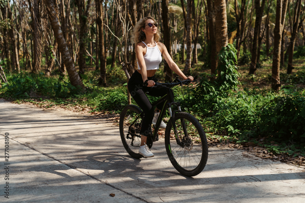 Pretty woman with Bicycle on a background of palm trees forest. Young girl riding bike in Vietnam or Thailand tropical jungle with coconut palms. Summer holiday tourist activity. Active sports tourism Pretty woman with Bicycle on a background of palm trees forest. Young girl riding bike in Vietnam or Thailand tropical jungle with coconut palms. Summer holiday tourist activity. Active sports tourism