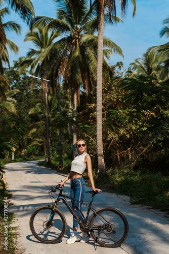 Pretty woman with Bicycle on a background of palm trees forest. Young girl riding bike in Vietnam or Thailand tropical jungle with coconut palms. Summer holiday tourist activity. Active sports tourism