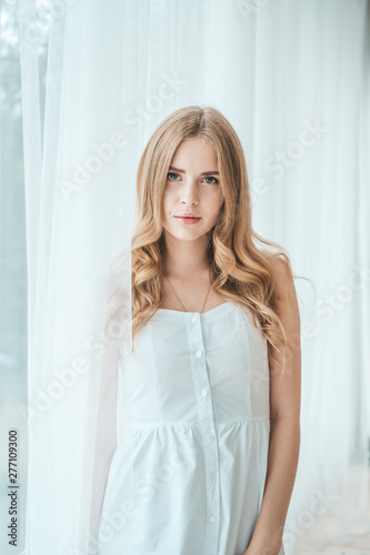 Girl in a light white dress posing by the window.