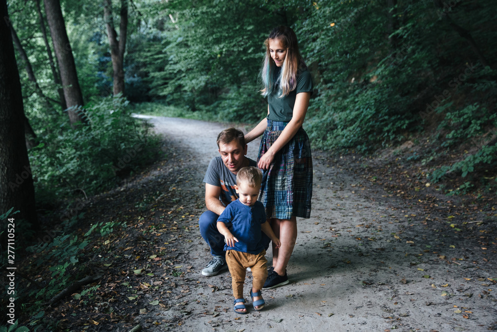 Happy young family father, mother and little son hugging and having fun outdoors, playing together in summer park