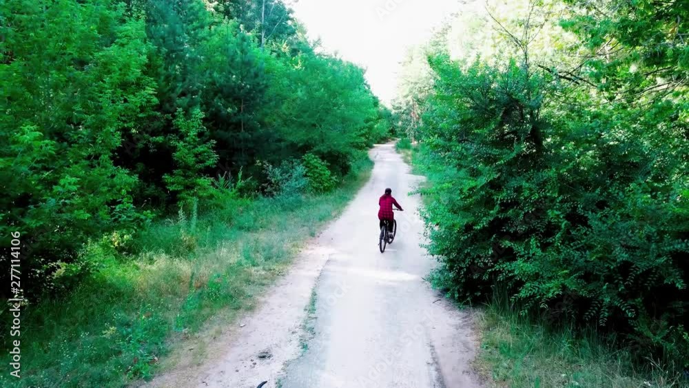 Girl riding a bike surrounded by green trees on a clear day, top view. Woman riding a bike in the woods Girl riding a bike surrounded by green trees on a clear day, top view. Woman riding a bike in the woods