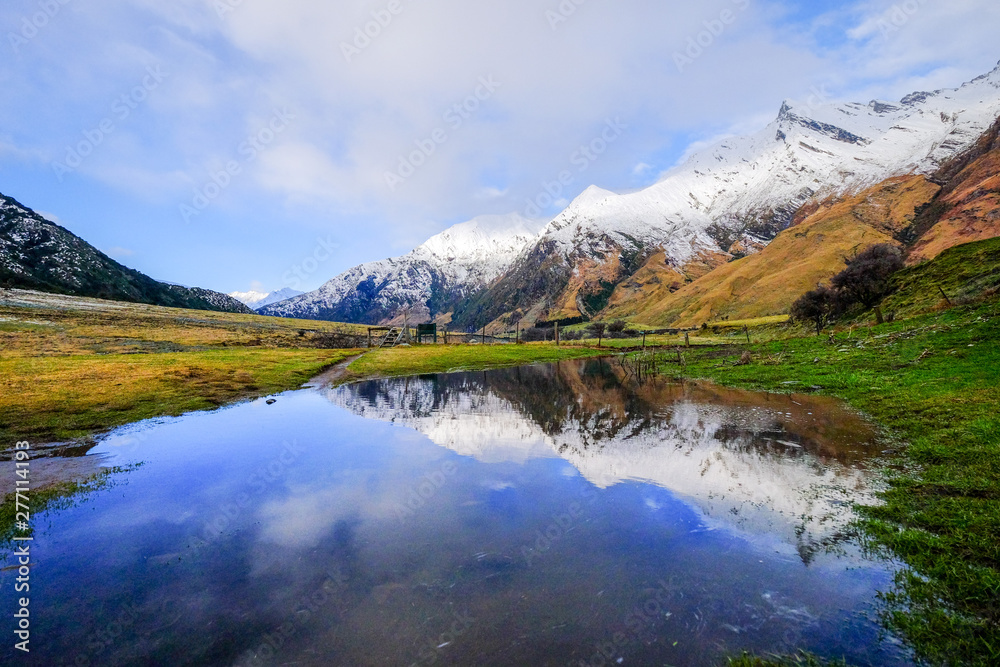 Natural landscape image of snow mountain, blue lake, green grass field in New Zealand. Peaceful remote image motivational and inspiration use.