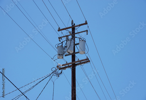 Electricity distribution pole with wiring cables and electrical equipment seen against a bright blue sky