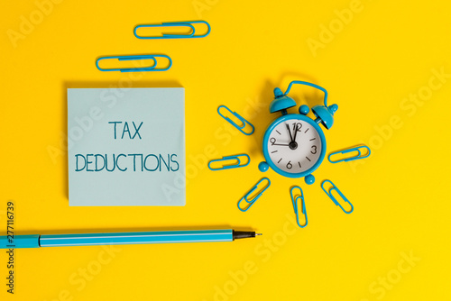 Word writing text Tax Deductions. Business photo showcasing an amount or cost that subtracted from someone s is income Metal alarm clock wakeup clips ballpoint notepad colored background photo
