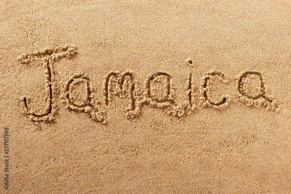 Fototapeta premium Jamaica word written in sand sign writing drawing drawn on a sunny summer beach holiday vacation travel destination message photo