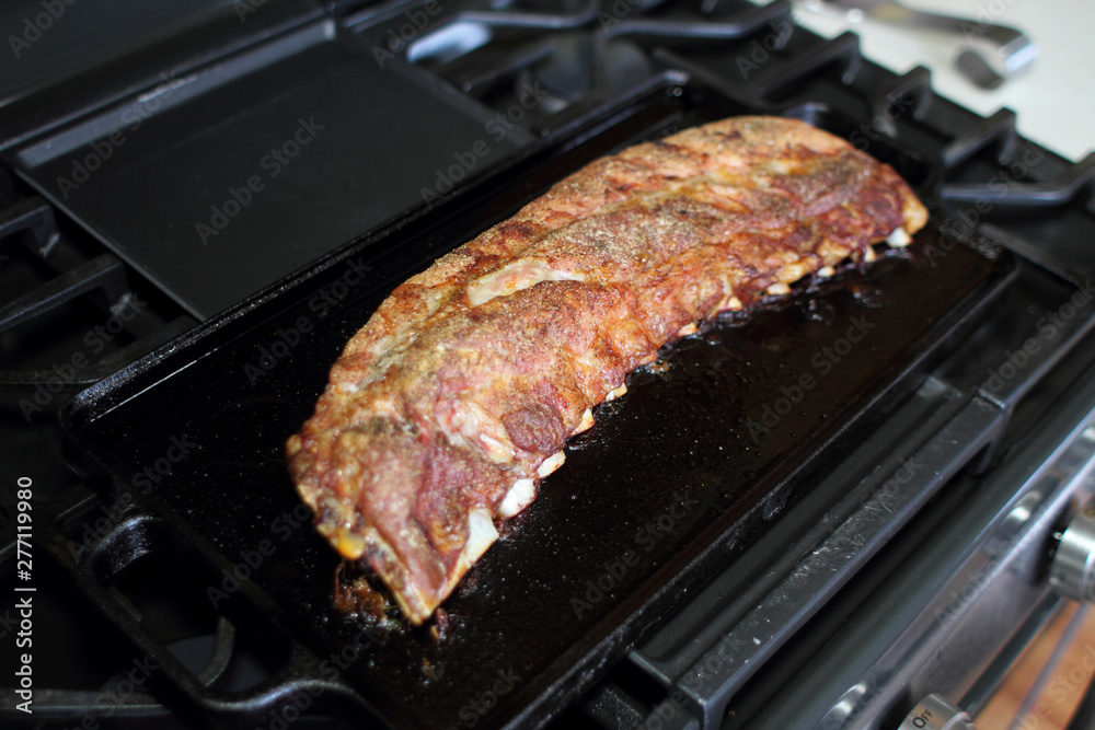Rack of dry rub pork ribs baked on a cast iron tray, resting on the stove top.