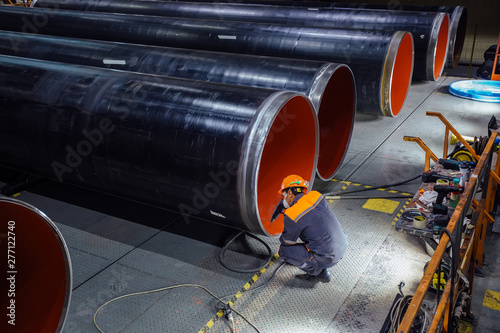 Billede på lærred Worker examines new coated pipe in factory