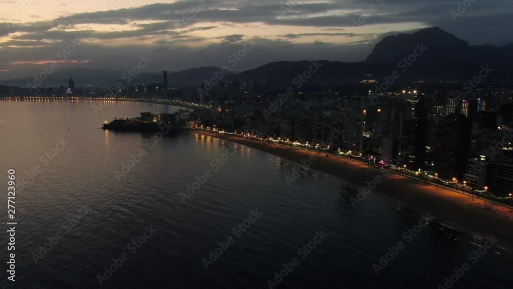 Beautiful blue hour aerial view of Benidorm, Spain. Peaceful beaches and smooth Mediterranean Sea with street lights glowing in the distance. DRONE BACKING and ASCENDING. Beautiful blue hour aerial view of Benidorm, Spain. Peaceful beaches and smooth Mediterranean Sea with street lights glowing in the distance. DRONE BACKING and ASCENDING.