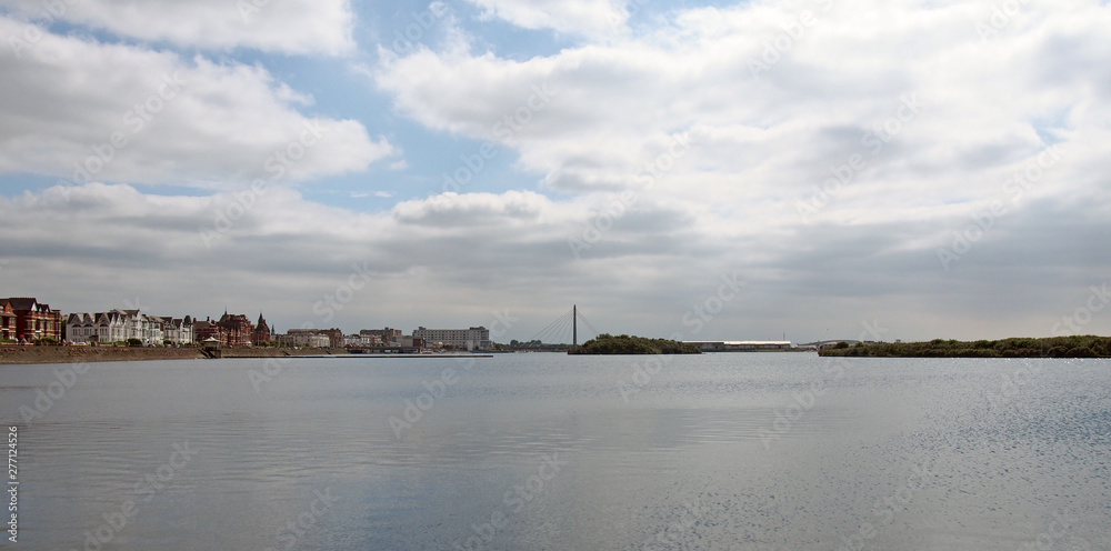 a wide panoramic view of the town of southport in merseyside from the sea with buildings along the waterfront and the bridge and pier in the distance