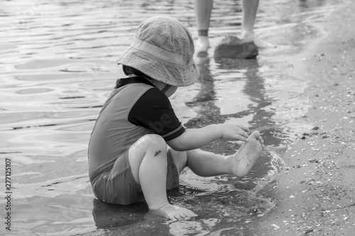 Young child playing in water at beach wearing playsuit and bucket hat photo