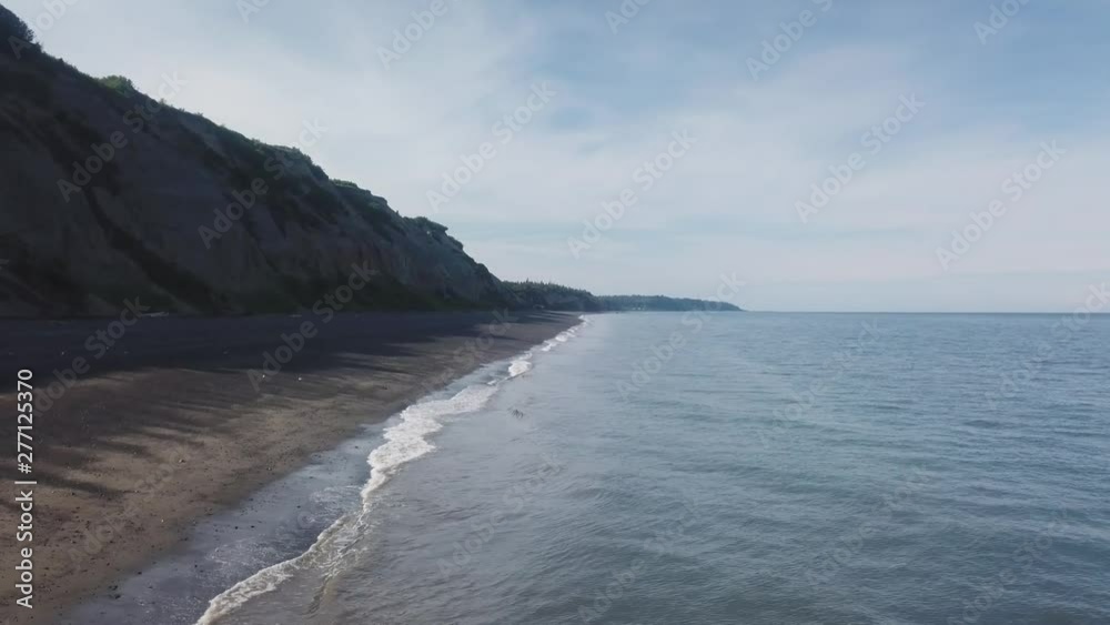 POV drone; Aerial view of a beautiful day at the beach at low tide near Clam Gulch, Alaska; sand, waves and green cliffs are visible POV drone; Aerial view of a beautiful day at the beach at low tide near Clam Gulch, Alaska; sand, waves and green cliffs are visible