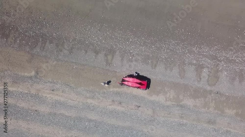 POV Drone; aerial view with descending perspective over a white Labrador dog, and an older Caucasian couple and their red off road vehicle; at low tide near Clam Gulch, Alaska photo
