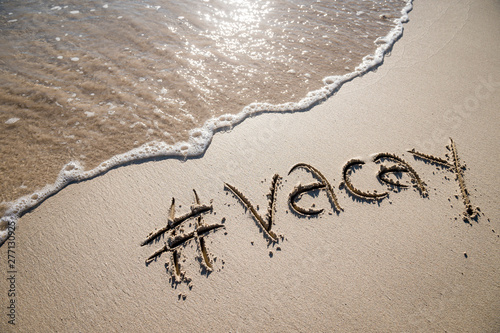 Modern travel message for the beach with a social media-friendly hashtag written with the word "vacay" in smooth sand with incoming wave