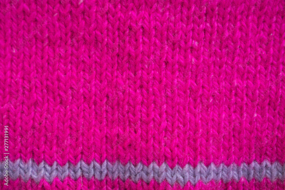 Magenta knitted horizontal textured winter background. Fragment of a bright pink color tied to the needles of a children's sweater with a purple strip. Texture, top view