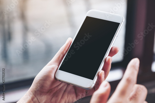 Mockup image of a woman holding white mobile phone with blank desktop screen in cafe